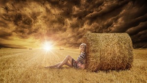 Woman resting against a hay bale on a hot summer's day